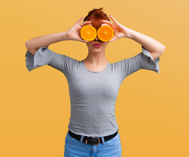 Young redhead girl wearing orange slices as glasses on orange background - 写真・画像