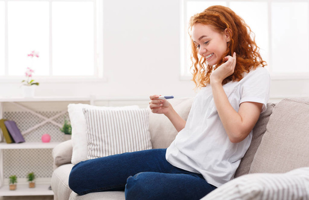 Szczęśliwa dziewczyna z testu ciążowego, siedząc na kanapie - Zdjęcie, obraz