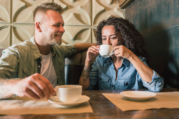 Happy young couple is drinking coffee and smiling while sitting at the cafe - 写真・画像