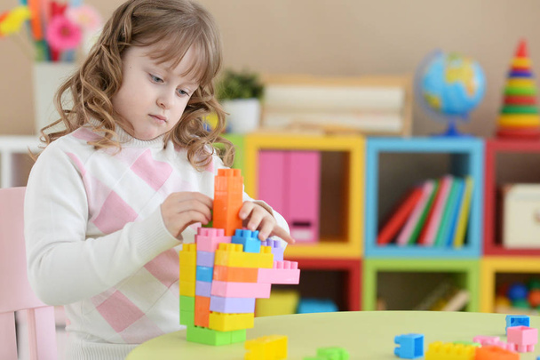 Curly little girl playing with colorful plastic blocks at her room - Фото, изображение