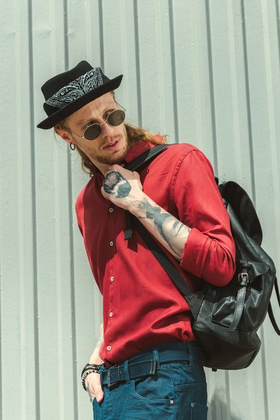 stylischer tätowierter Mann mit Sonnenbrille und Hut mit Rucksack - Foto, Bild