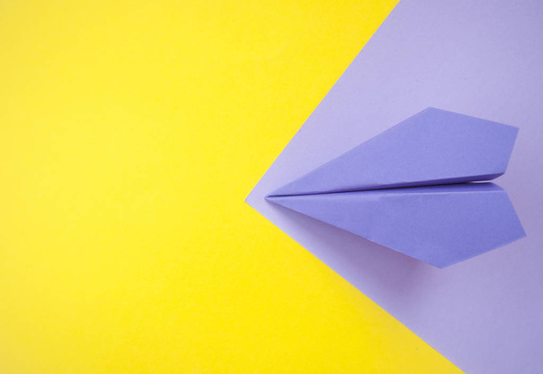 Επίπεδη στρώνουμε χαρτί αεροπλάνο σε φωτεινό κίτρινο και μοβ φόντο με κείμενο χώρο. - Φωτογραφία, εικόνα