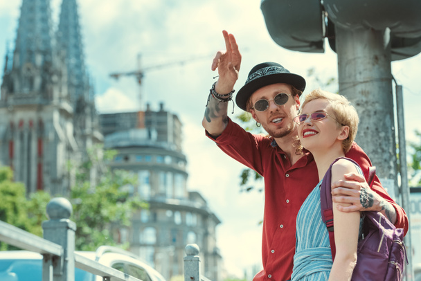 smiling stylish couple of tourists pointing at something in city - Photo, Image