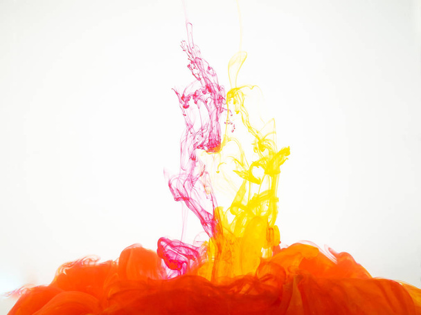 Yellow and red ink dropped into water and photographed while in motion. Colourful paint explosion under water isolated on white background. Ink splash isolated on white background. - Foto, Imagem
