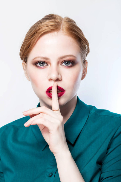 Beautiful model girl with redhead hair. Red lips. Woman holds a finger on her mouth a secret. Beauty, facial care, fashion, clean skin concept - Zdjęcie, obraz