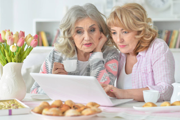 two  Senior women using laptop while drinking tea at kitchen - Foto, Bild