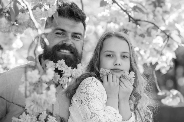 Child and man with tender pink flowers in beard. Childhood concept. Father and daughter on happy faces play with flowers, sakura background. Girl with dad near sakura flowers on spring day - Foto, Imagem