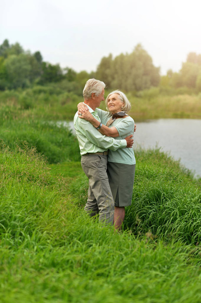 Loving senior couple dancing near lake in summer - Foto, imagen