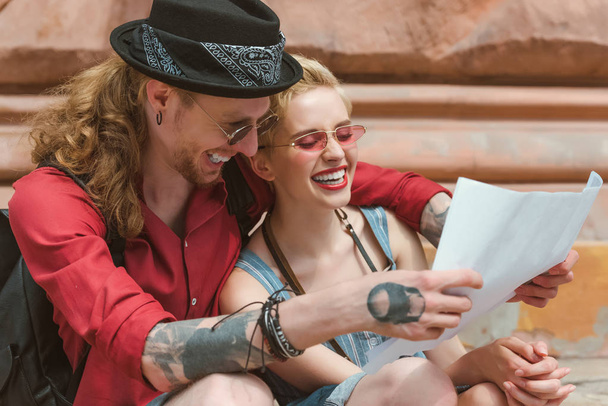 couple of young tourists laughing and looking at map in city - Фото, изображение