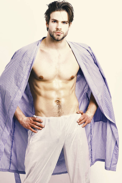 Muscular guy with torso and six packs in home or bath clothes. Morning and masculinity concept. Macho in blue bathrobe with strong fit body. Man with beard in blue dressing gown on white background - Фото, изображение