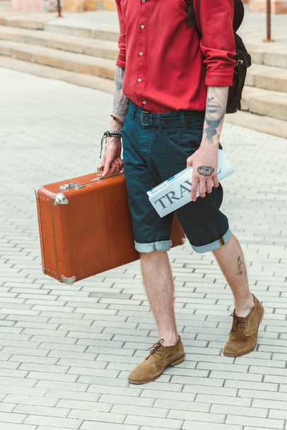 cropped view of man with travel newspaper and vintage suitcase - Zdjęcie, obraz