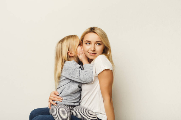 Little daughter whispering secret to her mother at white background - Photo, image