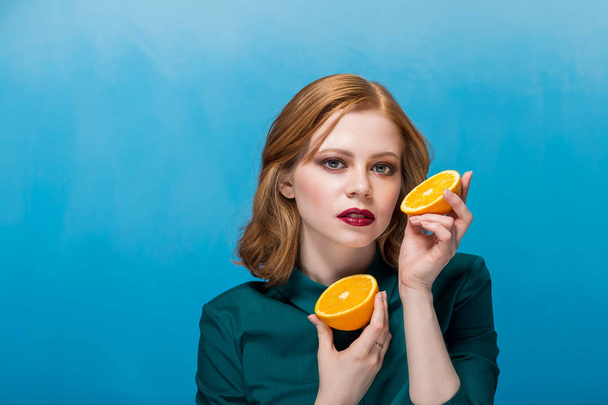 Beautiful woman with oranges on hand on blue background - Foto, afbeelding