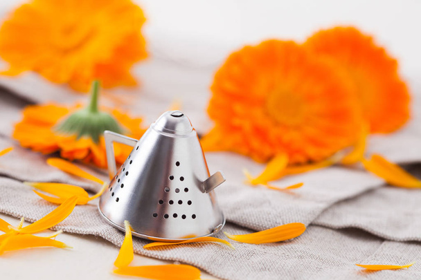 fiori di calendula arancione con cucchiaino infusore di tè in forma di bollitore sulla tovaglia, concetto di medicina a base di erbe
  - Foto, immagini