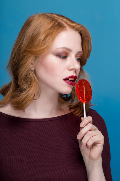 The girl holding a red lollipop. Valentines Day. Advertising. Girl holding a lollipop in his mouth. blue background - Fotoğraf, Görsel