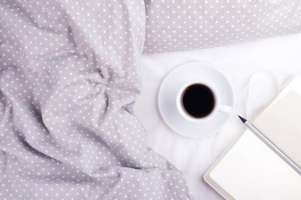 Het kopje koffie en papier notebook op bed. - Foto, afbeelding