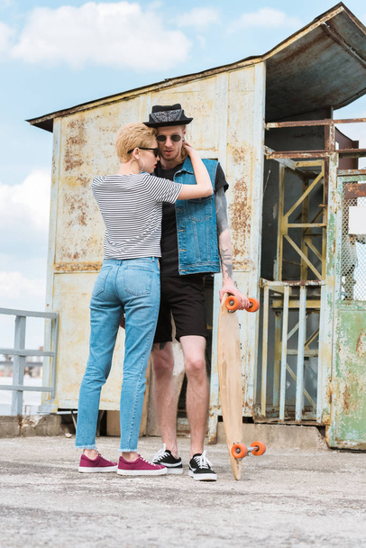 stylish girlfriend hugging tattooed boyfriend with skateboard - Photo, Image