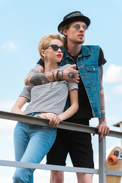 boyfriend with tattoos hugging stylish girlfriend and they leaning on railing - Photo, Image