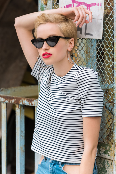stylish girl in sunglasses and with short hair posing near fence - Fotó, kép