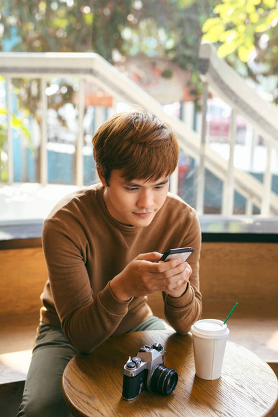 junger asiatischer Mann mit Smartphone beim Frühstück, Kaffee und Sommerurlaub - Foto, Bild