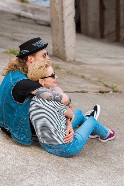 side view of boyfriend with tattoos hugging stylish girlfriend and they looking away - Zdjęcie, obraz