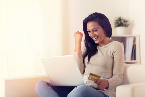 Muotokuva iloinen nainen käyttää kannettavaa tietokonetta ja ostaa verkossa luottokortilla sohvalla kotona
 - Valokuva, kuva
