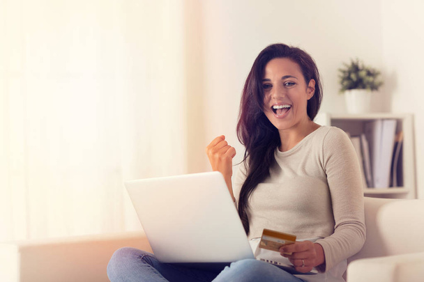 Portret van blijde vrouw met laptop en online met credit card op een bank thuis kopen - Foto, afbeelding