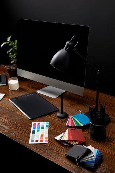 Nahaufnahme des Grafikdesignerarbeitsplatzes mit bunter Palette, Grafik-Tablet, leerem Computerbildschirm und Lampe auf Holzoberfläche - Foto, Bild