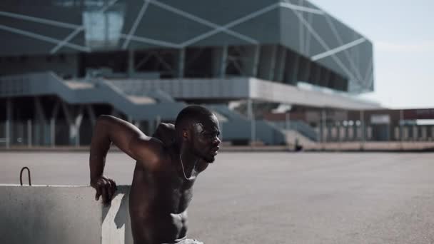 Street workout. Athletic African American man doing push-ups and spin exercise on outdoors. A black man is playing sports near the stadium. Workout, fitness, running, motivation - Footage, Video