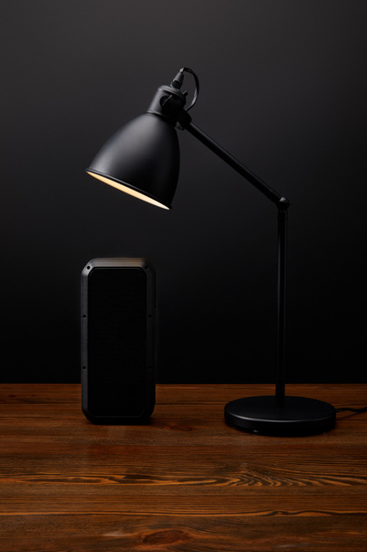 vista de cerca del altavoz de audio negro y la lámpara en la superficie de madera sobre fondo de pared negro
 - Foto, imagen
