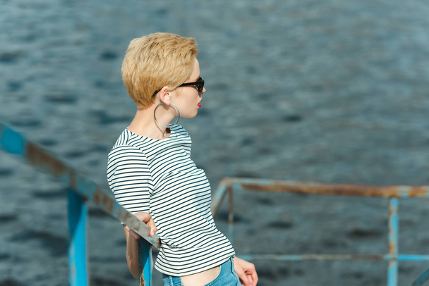 stylish girl in sunglasses leaning on railing near river and looking away - Photo, image
