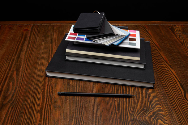 close up view of black notebooks, colors pallet and pencil on wooden tabletop - Foto, immagini