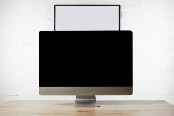close up view of designer workplace with blank computer screen on wooden surface and empty white board on brick wall - Photo, Image