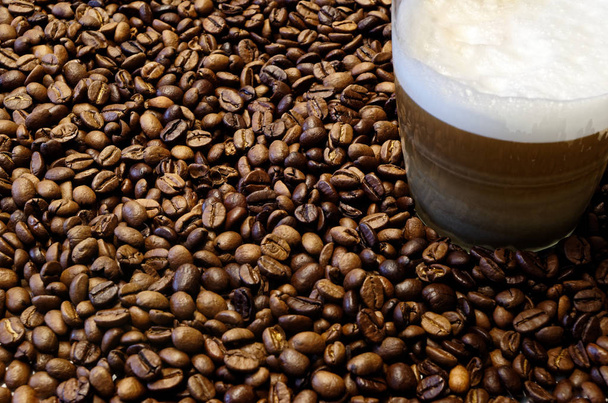 Roasted coffee beans are laid out as a background with a glass cup with a coffee in a corner - Photo, Image