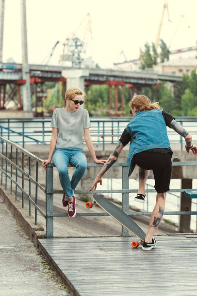 tattooed boyfriend skating in front of stylish girlfriend - Zdjęcie, obraz