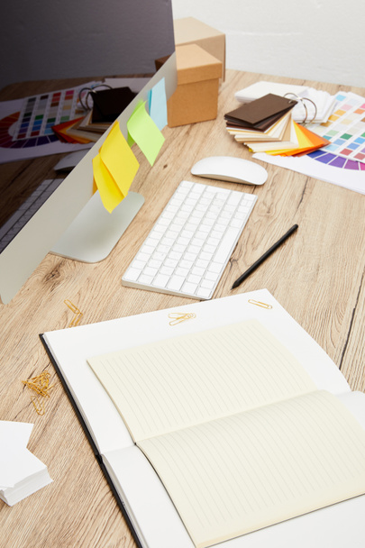 Close-up van ontwerper werkplek met computerscherm met kleurrijke stickers, notitieboekjes en pallet op houten tafelblad - Foto, afbeelding
