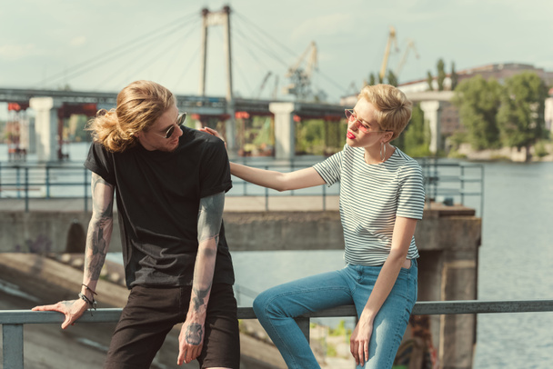 stylish girlfriend palming boyfriend with tattoos on bridge - Foto, Imagen
