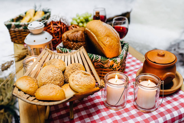 Összetétele friss kenyeret, fa állványon és gyertyák, vörösboros pohár a háttérben. Téli piknik az erdőben - Fotó, kép