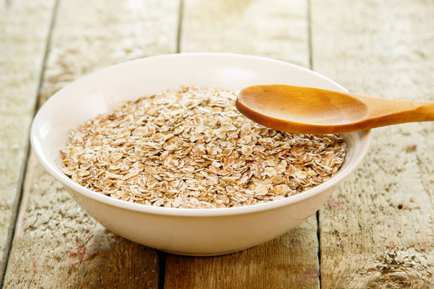 Uncooked oatmeal and wooden spoon. The best grain for breakfast. - Foto, Imagen