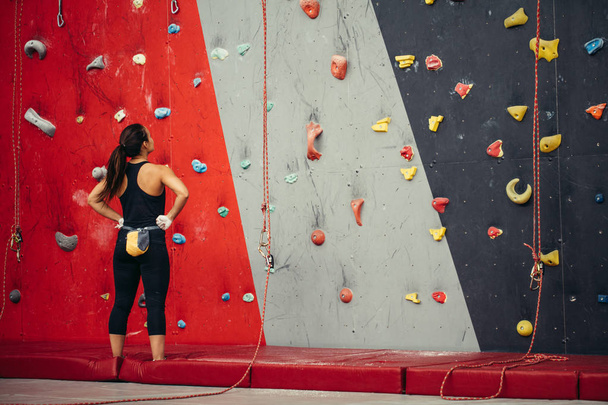 Sportswoman looking at climbing wall in gym - Fotoğraf, Görsel