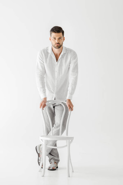 young man in linen clothes standing near chair isolated on grey background  - Фото, изображение