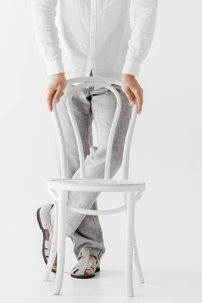 imagem cortada do modelo masculino em roupas de linho em pé perto da cadeira isolada no fundo cinza
  - Foto, Imagem