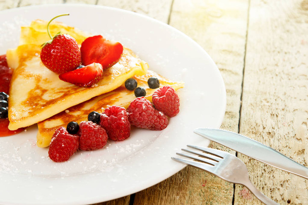 Pancakes with fresh berries and sugar powder on wooden table - Fotó, kép