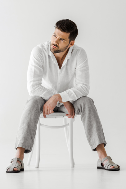 confident man in linen clothes sitting on chair and looking away isolated on grey background  - Foto, immagini