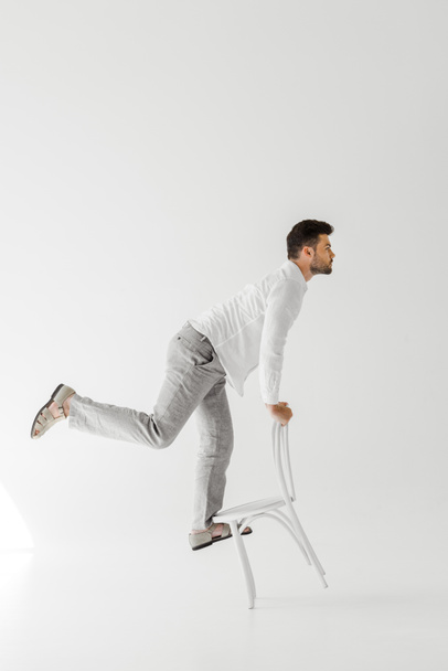 sivunäkymä mies pellava vaatteet tasapainotus tuolilla eristetty harmaalla pohjalla
  - Valokuva, kuva
