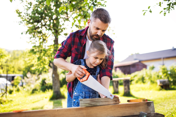Father and a small daughter with a saw outside, making wooden birdhouse. - 写真・画像