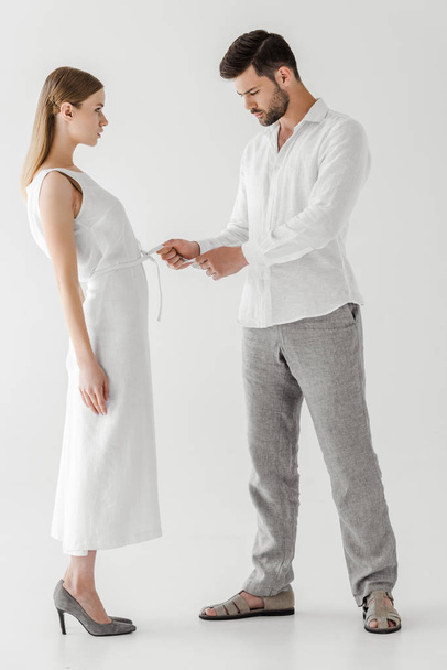 side view of male model untying white linen dress of girlfriend isolated on grey background  - Photo, Image
