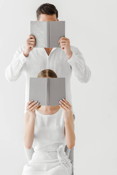 couple in linen clothes covering faces by books isolated on grey background  - Zdjęcie, obraz