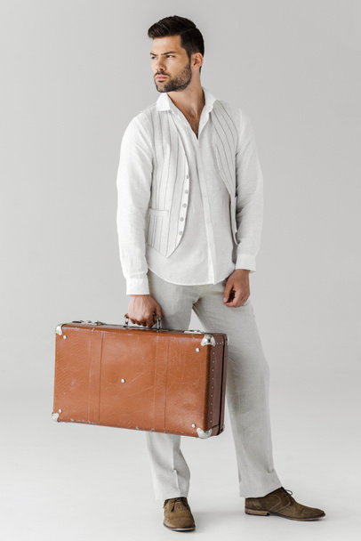 serious stylish male traveler in linen clothes holding vintage suitcase isolated on grey background  - Fotoğraf, Görsel
