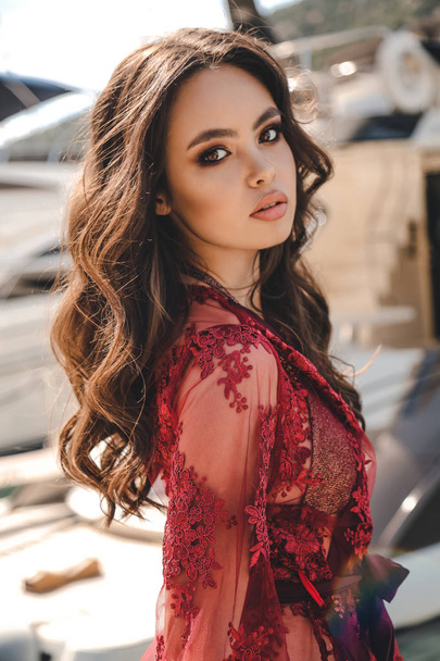 fashion outdoor photo of beautiful young woman with dark hair in elegant red dress posing near yachts in pier - Photo, image